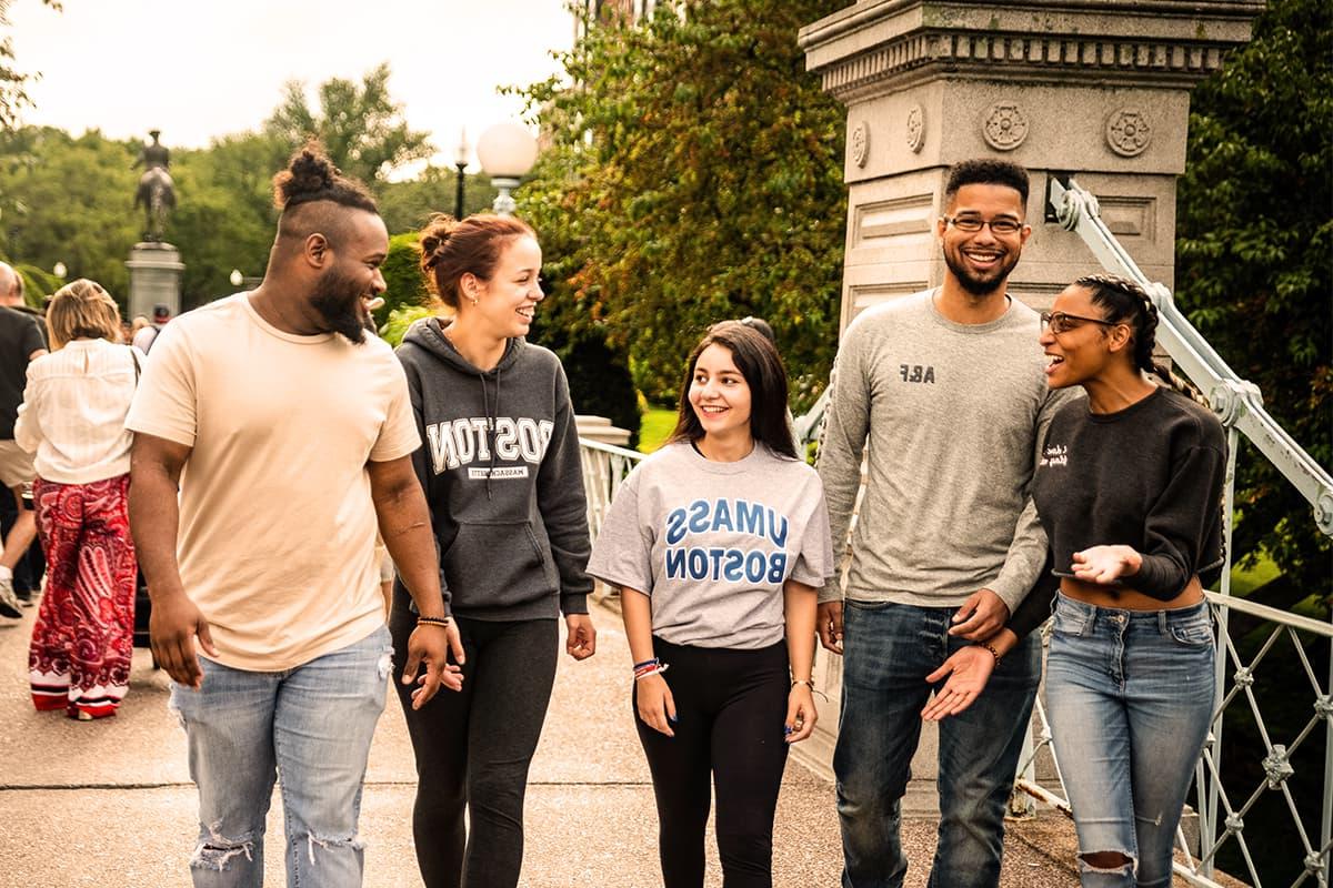 4 students in UMB apparel walk in the Boston Public Gardens past the gates.